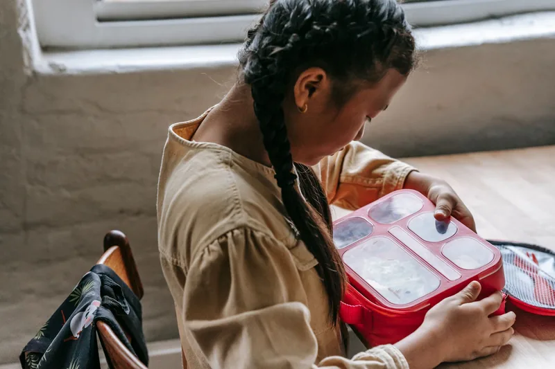 Child packing a labeled lunch box the night before summer camp